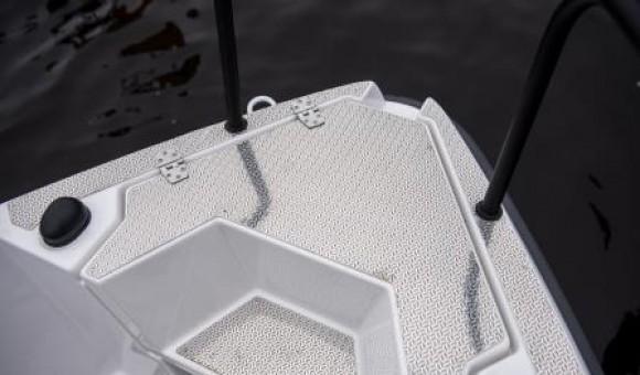 White boat deck showing textured flooring and two black handrails, with dark water in the background.